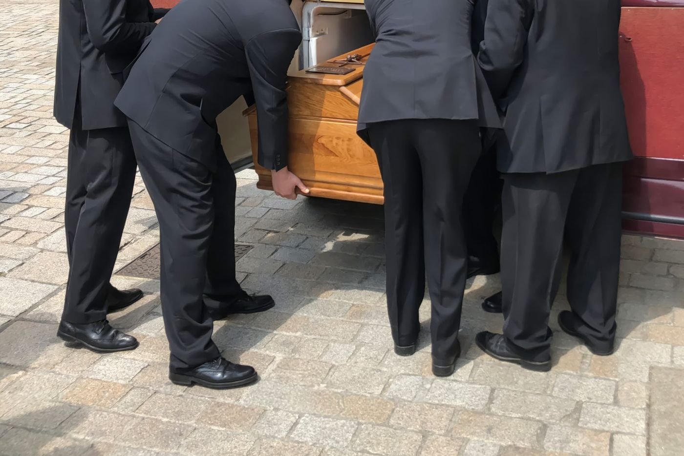 Pallbearers in dark suits carrying a casket home: a death far from home, met together